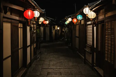 A quiet night alley with glowing paper lanterns hanging between traditional wooden buildings.