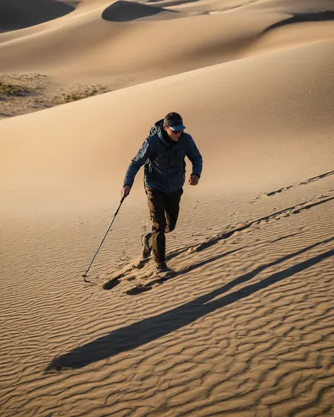Hiker climbing sand dune with trekking pole at golden hour