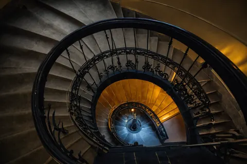 Spiral staircase with black iron railings descending into warm golden light