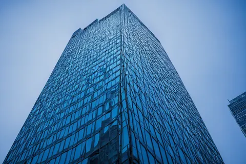 Towering glass skyscraper reflecting cityscape against blue sky