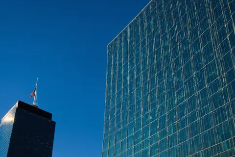 Two glass skyscrapers with an American flag on one tower under a clear blue sky